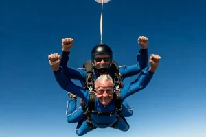 A older man midair during a tandem skydive with another man for his 70th milestone birthday party activity