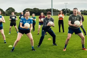 A group of adult men and women wearing sports clothing on a sports field and being taught Irish football (GAA) skills as a group activity