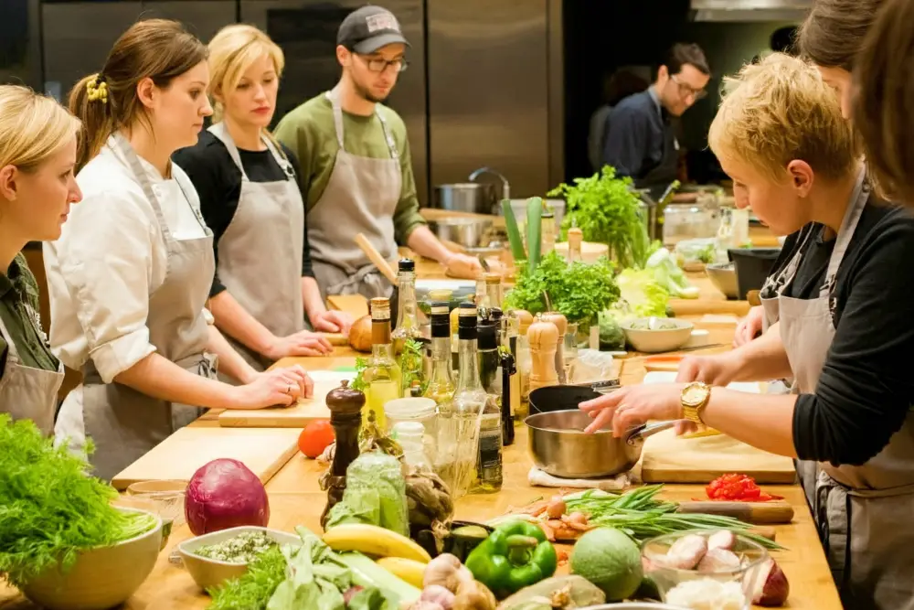 A group of young adults taking part in a cooking class with a teacher for a birthday party actvity