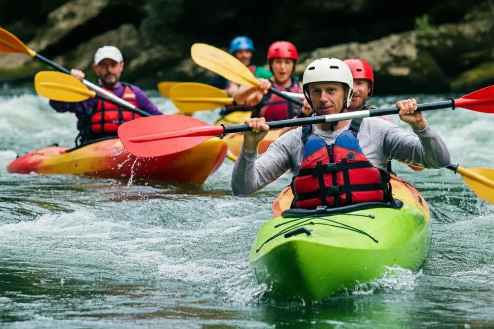 A group of adults in kayaks moving down rapids on a river for a group kayaking activity