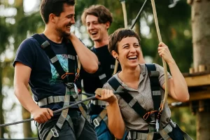 Three adults walking and laughing whilst up on a high ropes course in a forested area for a birthday party activity