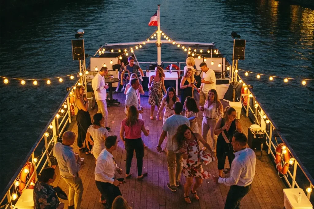 A large group of adults dancing on the deck of a boat on a river for company away days ideas